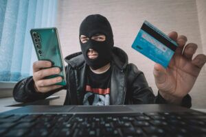 Man in a balaclava holding a credit card and smartphone, illustrating credit card fraud tactics, for Huff Insurance's blog on credit card fraud prevention